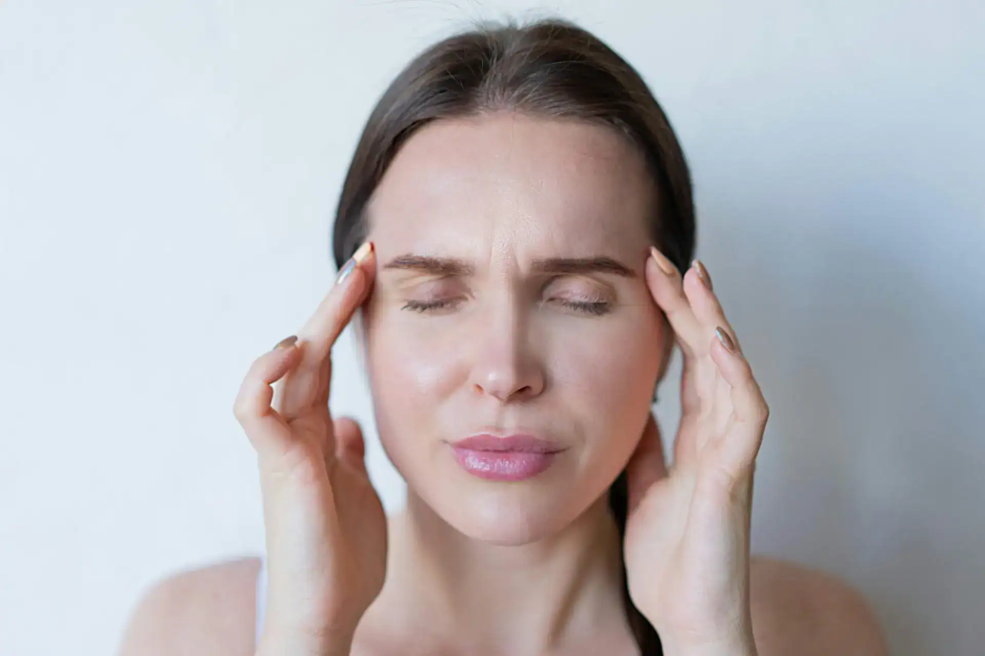 Close-up of a woman with closed eyes holding her temples, showing signs of a migraine or headache.