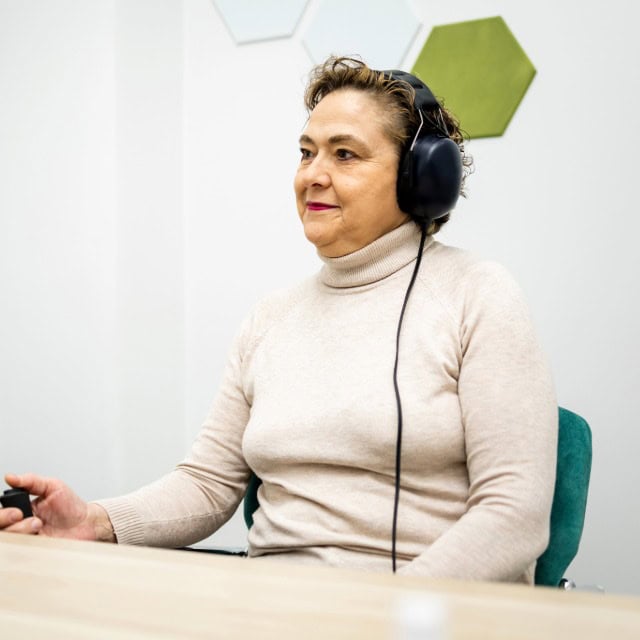 Older woman wearing audiometric headphones during a hearing test at AUDICOG in Houston